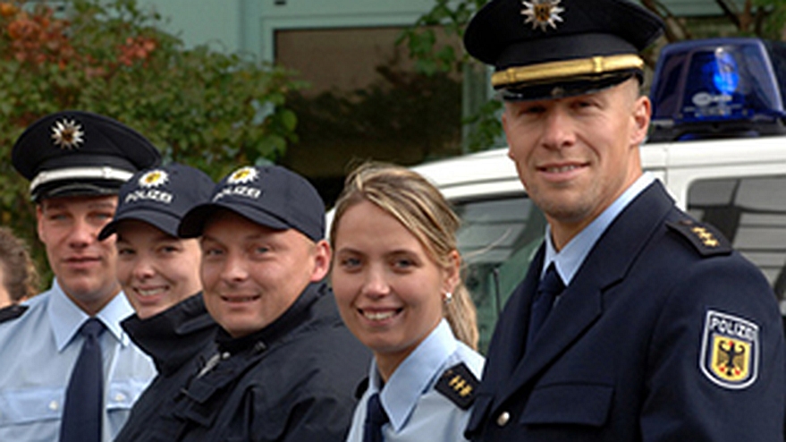 Mehrere Personen stehend vor einem Polizeiauto.
